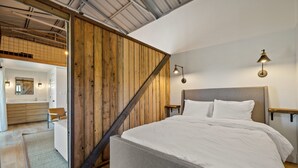 A bedroom with a large bed, wooden panel walls, and a loft area with a desk and chair. - Riverside Suite Casita 1 (Greer)