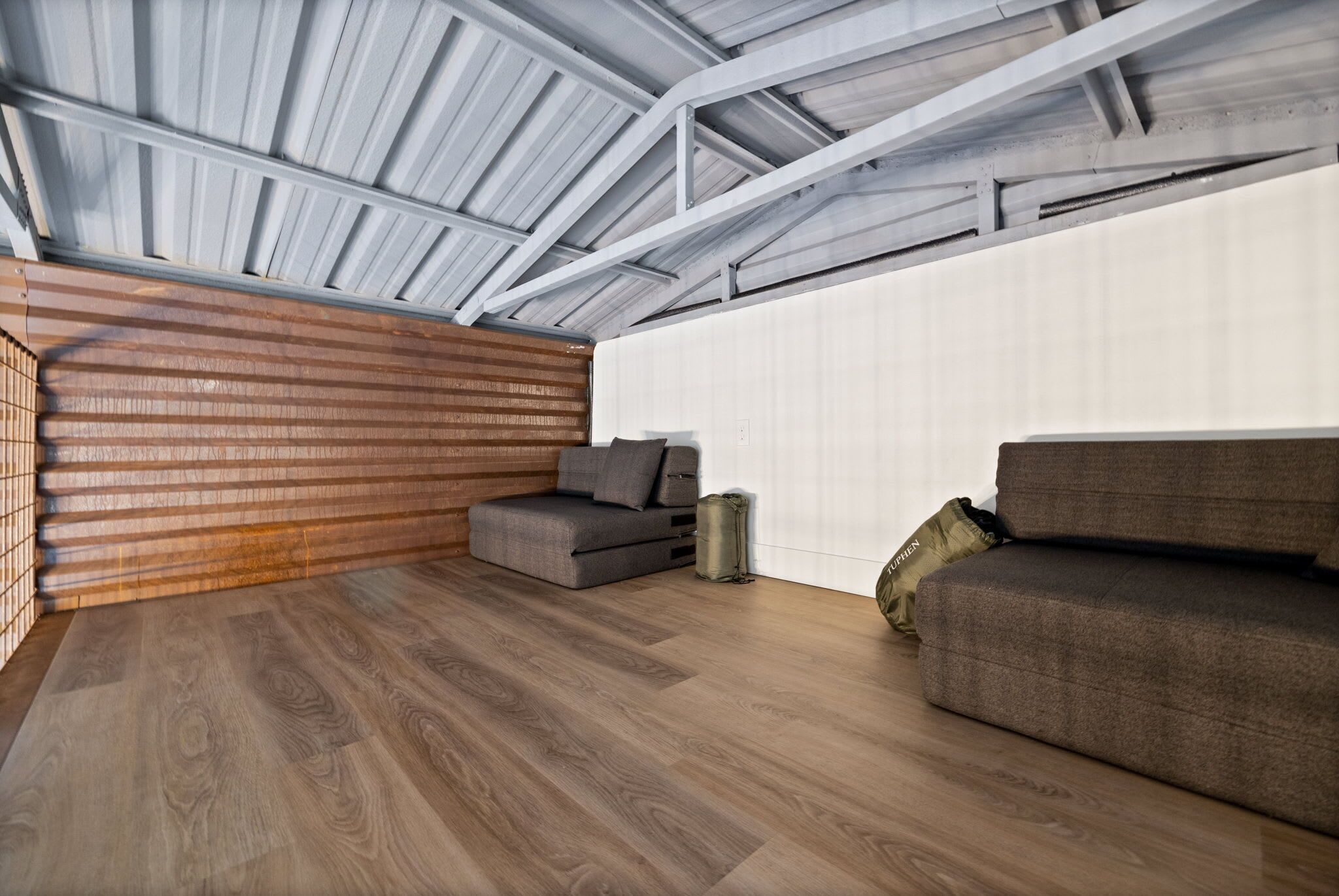 Une chambre moderne de style loft, avec un plafond en pente, un mur recouvert de lambris en bois et un grand canapé d’angle gris.