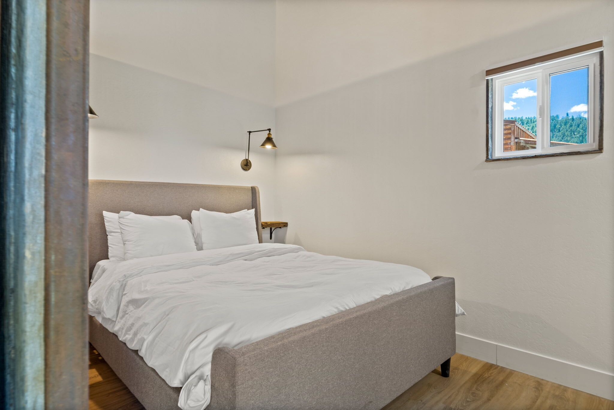 Un dormitorio con cama, mesita de noche, lámpara y ventana con vistas a árboles.