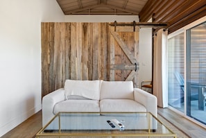Uma sala de estar moderna com sofá branco, mesa de centro de vidro e painel de parede de madeira.