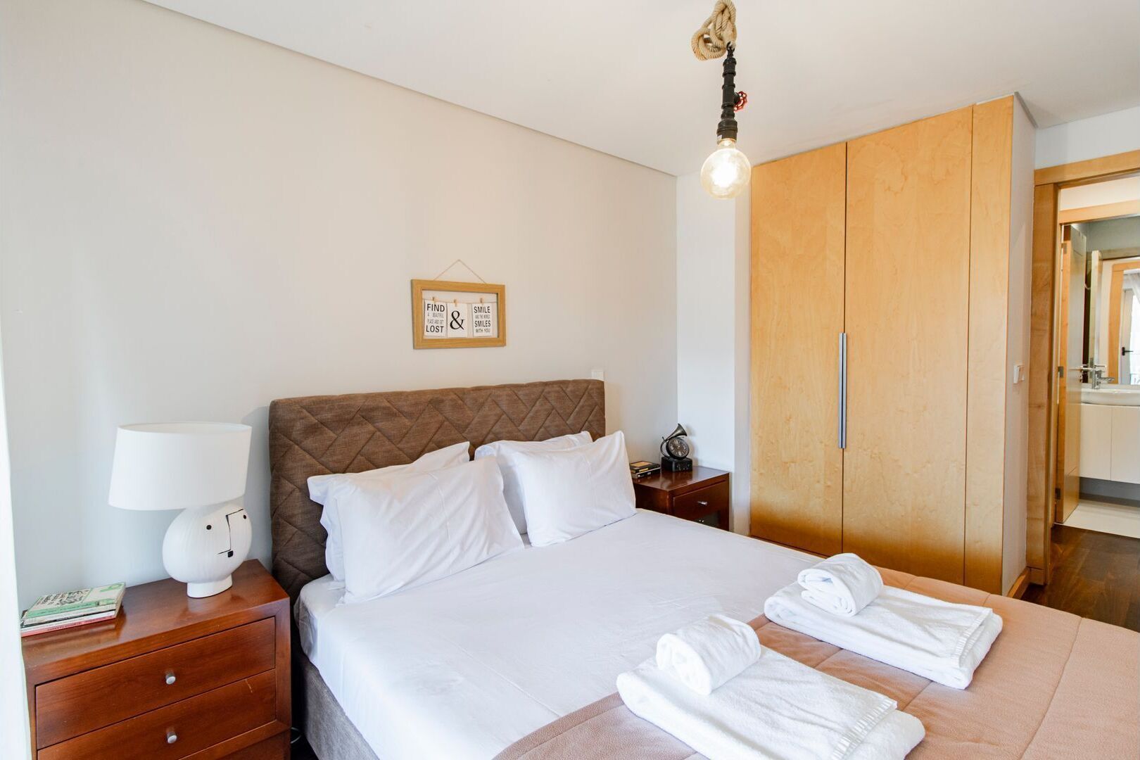 Une chambre d’hôtel avec un lit, une lampe de chevet, une armoire en bois et une citation inspirante encadrée au mur.