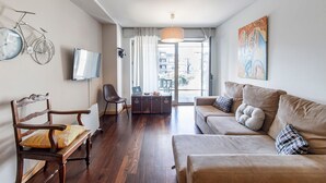 A living room with a wooden floor, a sofa, a chair, a television, and a bicycle wall art. - D. João IV Apartment w/ Terrace by LovelyStay (Porto)