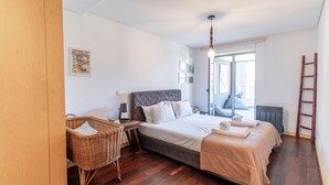 A bedroom with a bed, a bedside table, a lamp, a wicker chair, a ladder, and a window. - D. João IV Apartment w/ Terrace by LovelyStay (Porto)