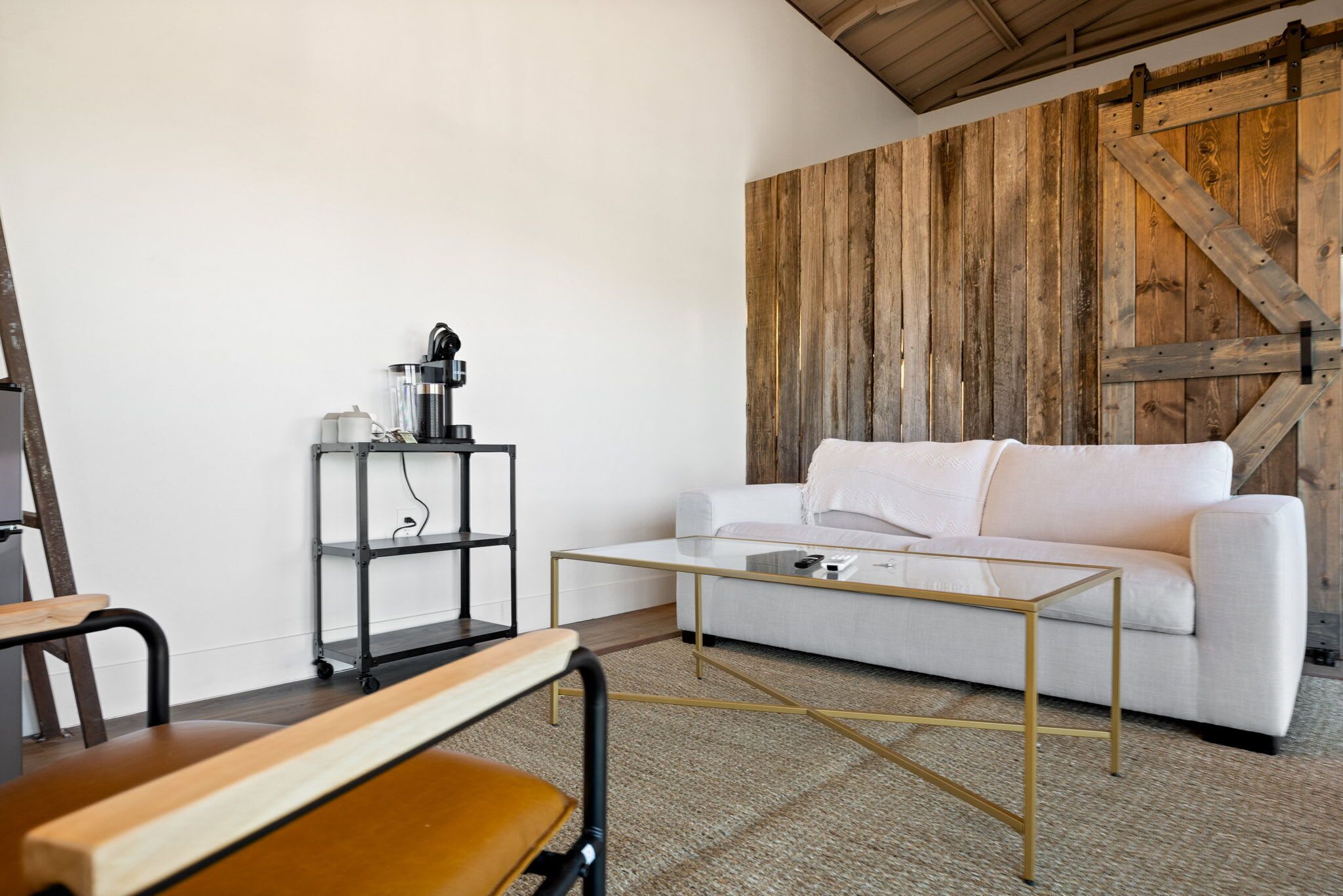 Een moderne woonkamer met een witte bank, een glazen salontafel en een houten wand.