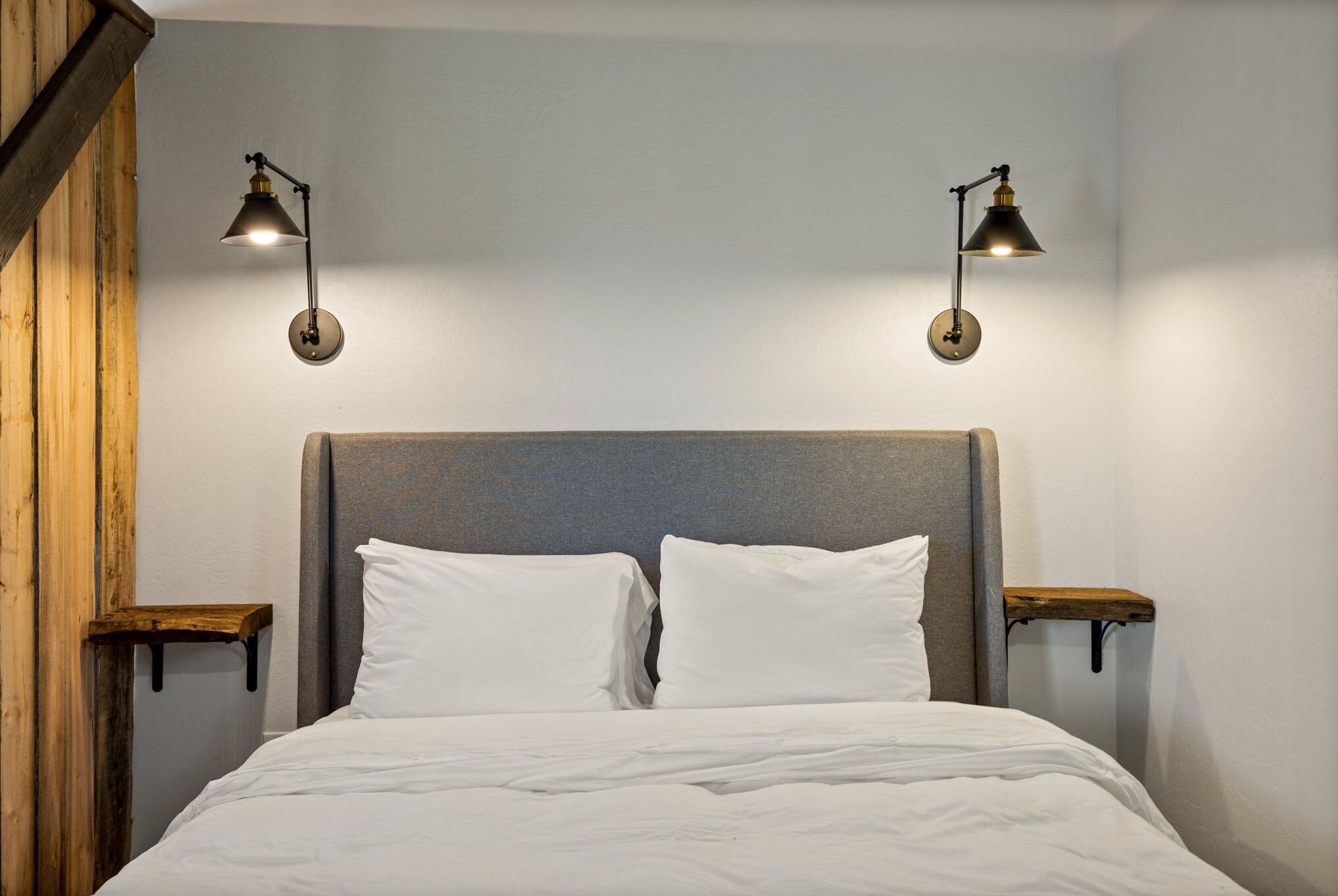 A neatly made bed with white linens, two wall-mounted reading lamps, and wooden nightstands.