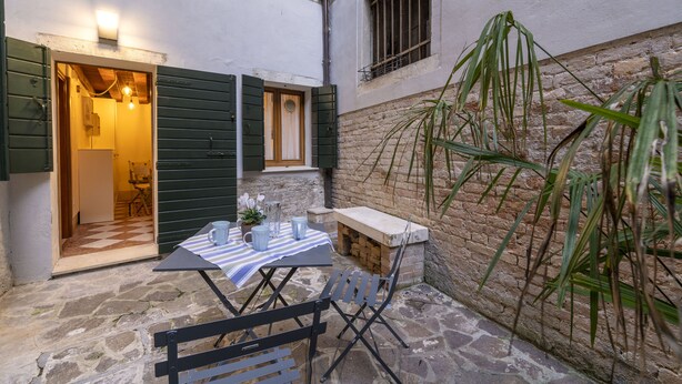 An outdoor patio with a table and chairs, a small bench, and a potted plant. - SAN SILVESTRO HOUSE VENICE (Venezia)