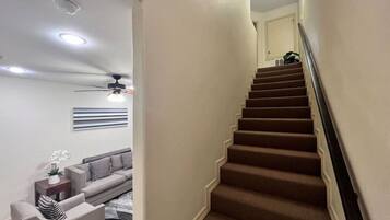 Eine Treppe mit Teppichstufen führt zu einer Zwischenebene, dort ist ein Deckenventilator und ein Sofa im angrenzenden Wohnbereich zu sehen.