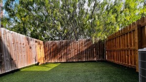 A backyard with artificial green grass, a wooden fence, and a concrete patio. - Nest at Hummingbird 3 w King bed free parking Patio. (Pharr)