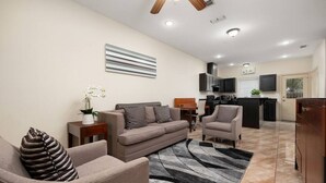 A modern living room with a sofa, armchairs, a coffee table, and a rug. There is a kitchen in the background with a TV and cabinets. - Nest at Hummingbird 3 w King bed free parking Patio. (Pharr)