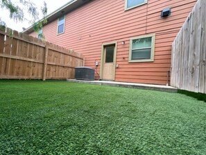 A backyard with artificial grass, a wooden fence, and a house with a door and windows. - Nest at Hummingbird 3 w King bed free parking  Patio (Pharr)