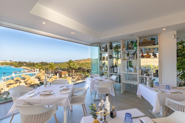 Un espace repas avec des tables préparées pour deux personnes, offrant une vue sur une piscine et un paysage pittoresque.