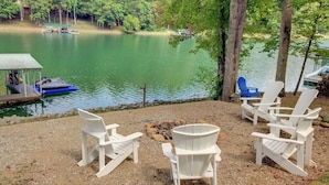 Ein Sitzbereich am Seeufer mit Adirondack-Stühlen und einer Anlegestelle mit einem Boot.