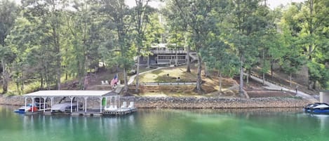 Una cabaña junto al lago con un muelle techado, rodeada de árboles densos.