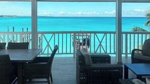 A covered outdoor area with a view of the ocean, featuring a table and chairs, a ceiling fan, and a railing. - Bahamas Beach House (Nassau)