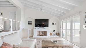 A spacious living room with a fireplace, a large TV, and a balcony with a view. - Bahamas Beach House (Nassau)