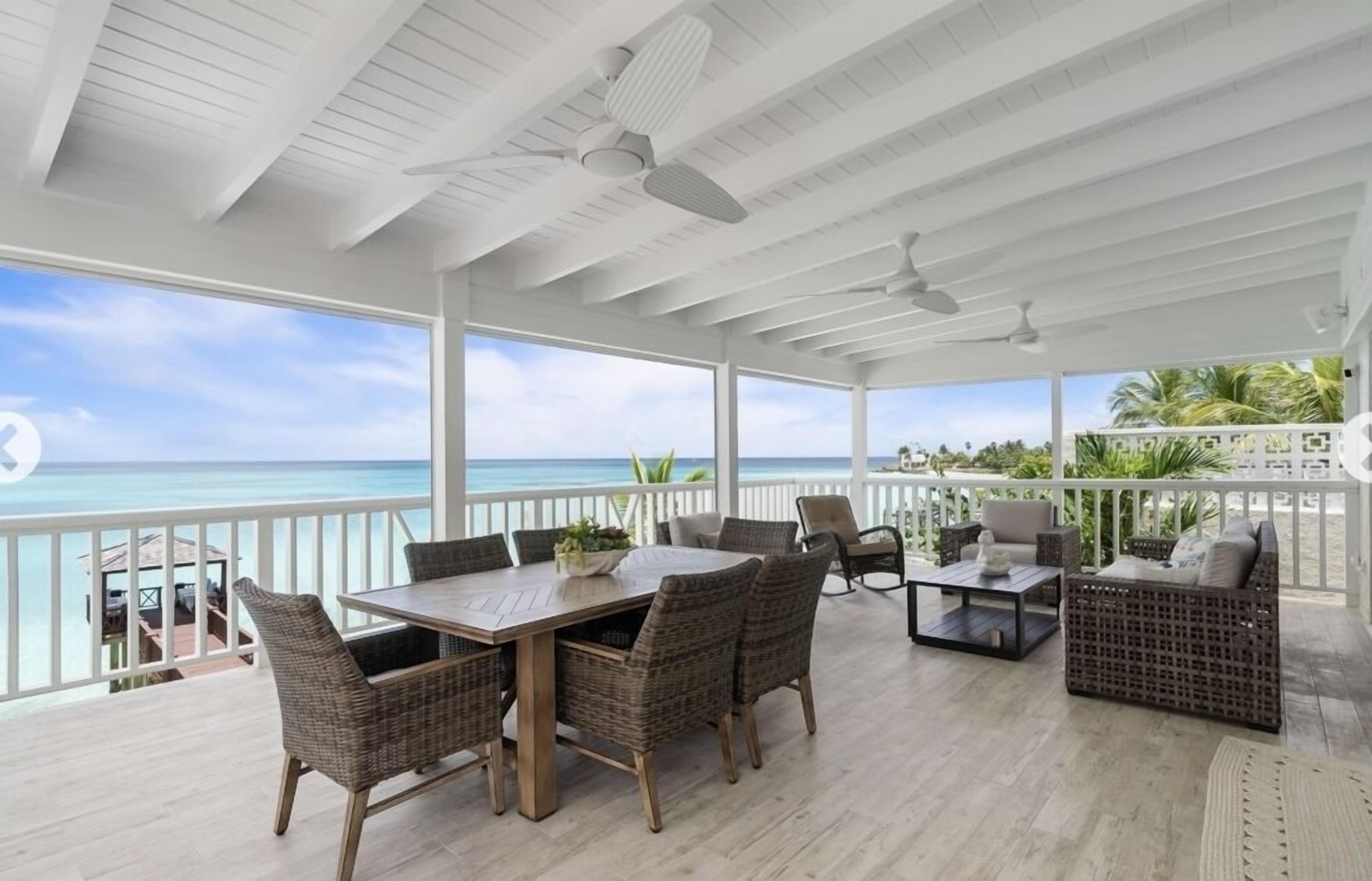 A covered outdoor area with a wooden table and wicker chairs, overlooking the ocean.