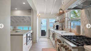 A modern kitchen with a large island, a gas stove, and a view of the ocean through a sliding door. - Bahamas Beach House (Nassau)