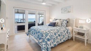 Ein Schlafzimmer mit Bett, Nachttisch, Schreibtisch und Meerblick durch eine Schiebetür.