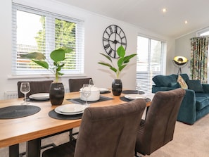 Un comedor con una mesa de madera, dos jarrones con plantas, un reloj de pared y un sofá azul al fondo.