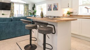 Una cocina moderna con una isla central, taburetes de bar, un televisor de pantalla plana y un comedor con un sofá azul.
