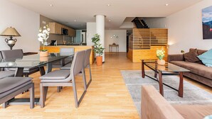 A modern living room with a glass dining table, grey sofas, and a wooden staircase. - Antara apartments by VH (Mexico City)