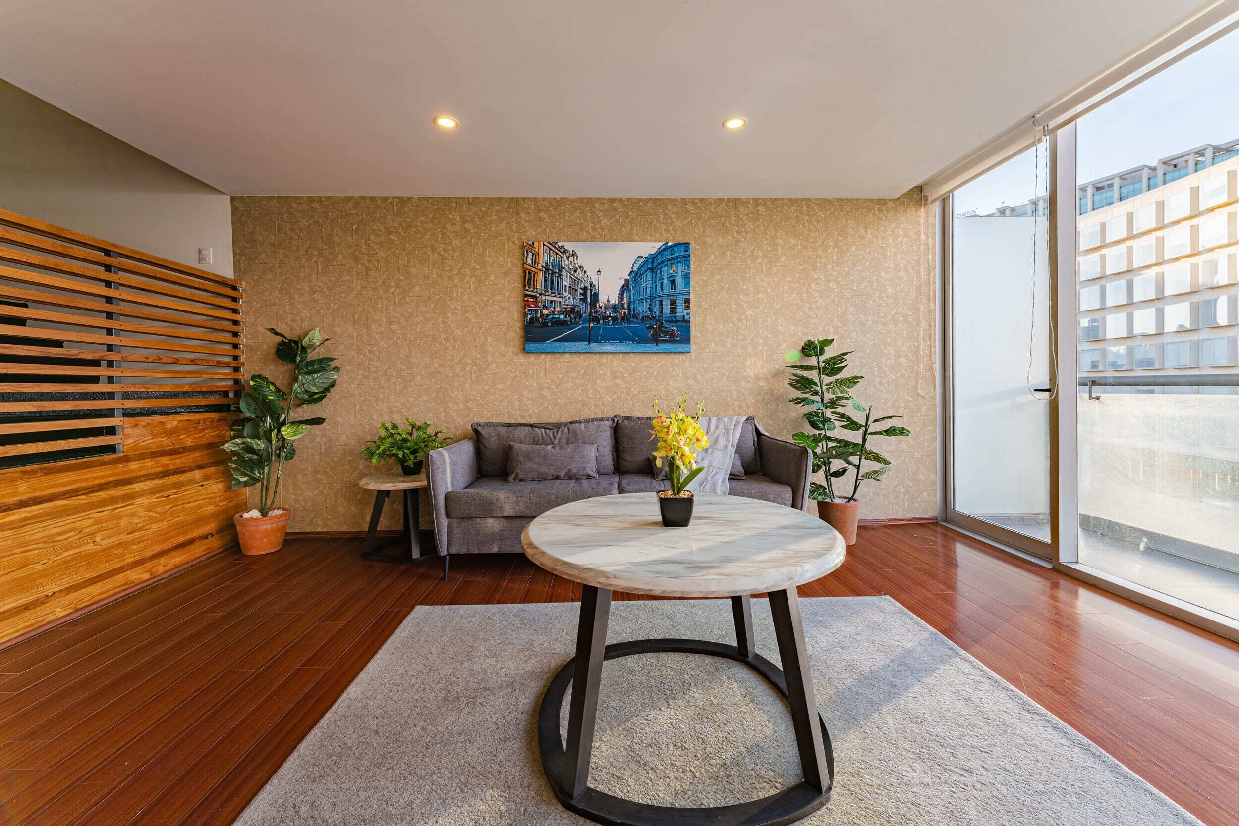 A modern living room with a sofa, a round table with a vase of flowers, and two potted plants.