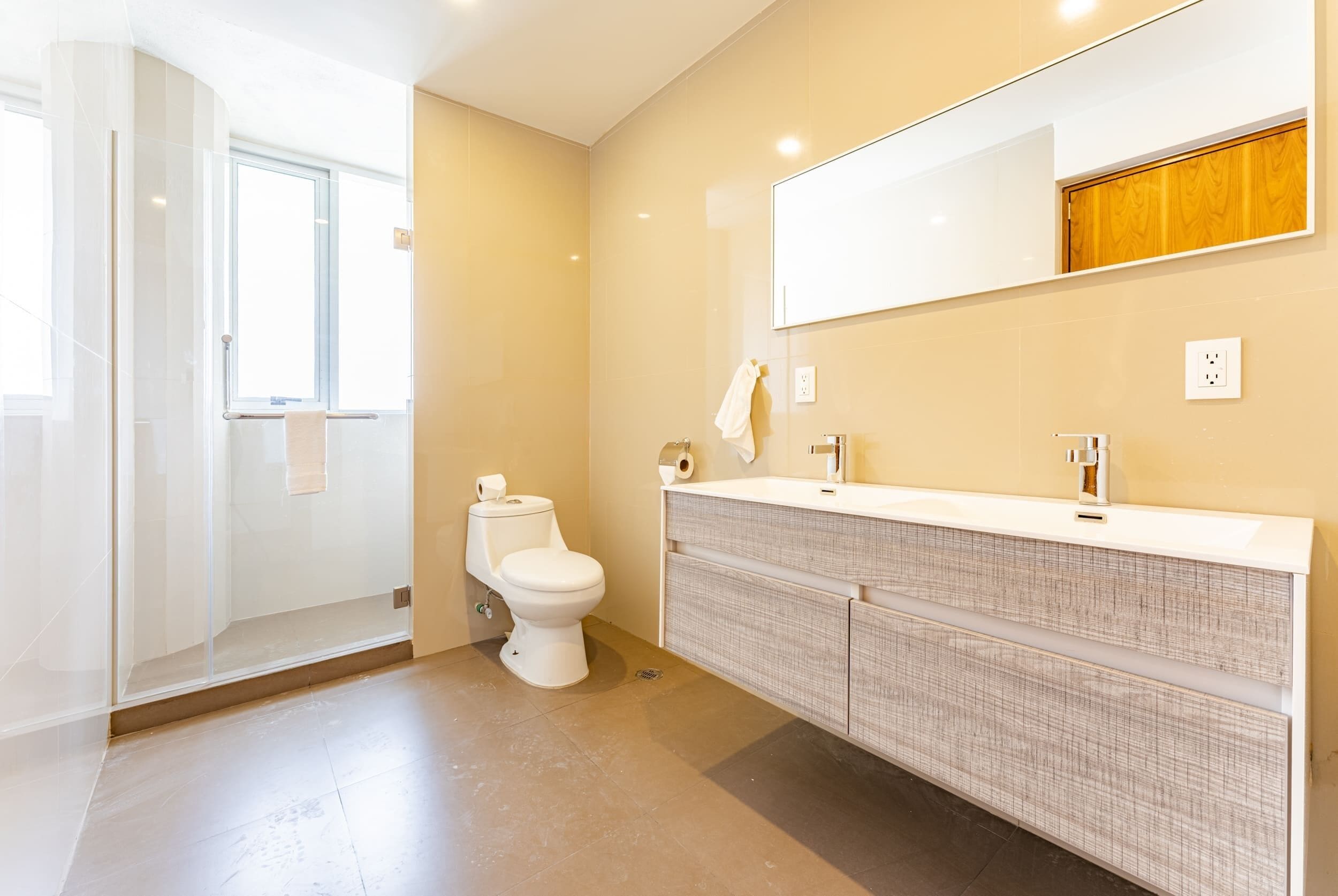 Un baño moderno con cabina de ducha de vidrio, inodoro blanco y un amplio lavamanos con espejo.