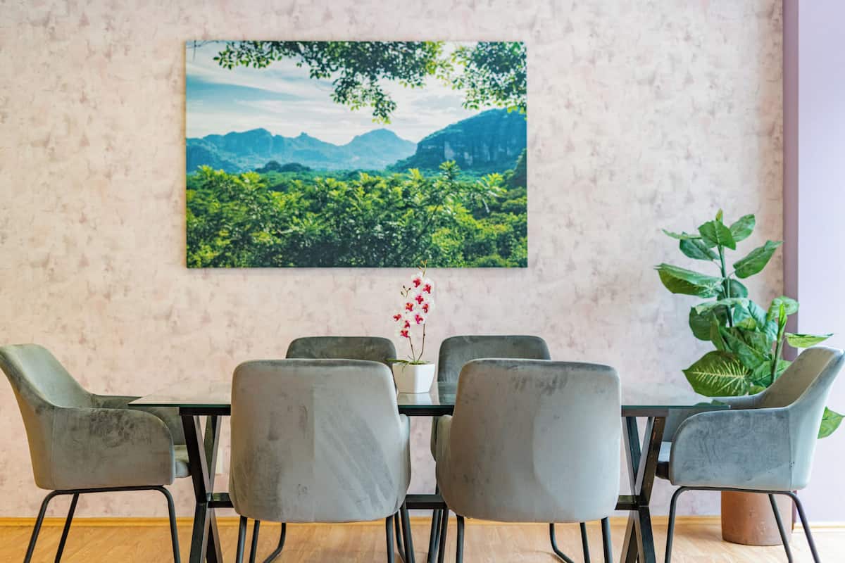 Un comedor con una mesa y seis sillas, una planta en maceta y un cuadro grande de paisaje en la pared.