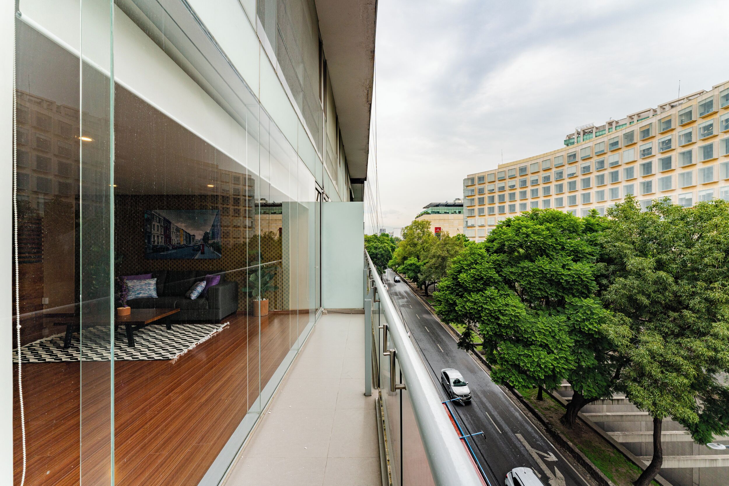A modern hotel room with a large glass window, a wooden floor, a sofa, and a coffee table.