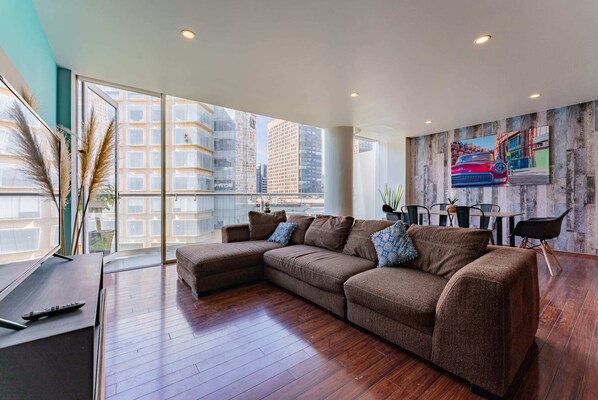 A modern living room with a large sectional sofa, a dining table with chairs, and a cityscape view through large windows.