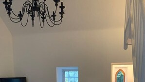 A living room with a television, a window with a plant, a chandelier, and a door with a window.