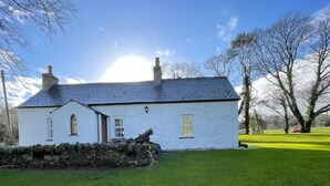 A white building with a stone wall in front, a sloped roof, and a clear sky.