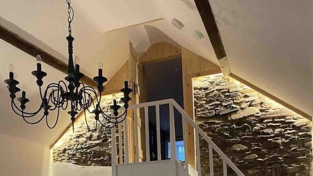 A living room with a white sofa, a striped throw blanket, a small round table, and a staircase leading to an upper level with a stone wall.