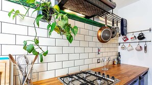 Una cocina con estufa a gas, ollas colgantes, un escurreplatos con utensilios de cocina y una planta en maceta.