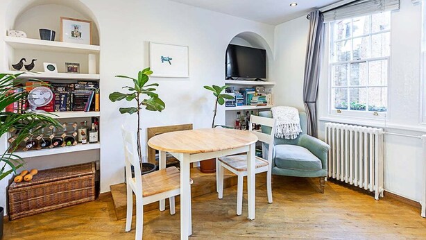 Un salón acogedor con una mesa y sillas de madera, un televisor y una estantería.