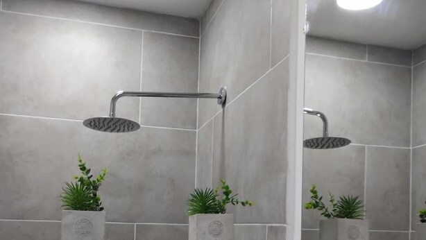 Une salle de bain moderne avec des carreaux gris, un mur d’accent en briques blanches et deux petites plantes en pot.