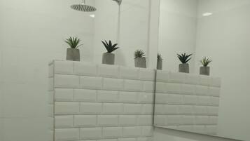 Un bagno con box doccia rivestito di piastrelle bianche, un WC e un lavandino. Sul box doccia ci sono piccole piante in vaso.