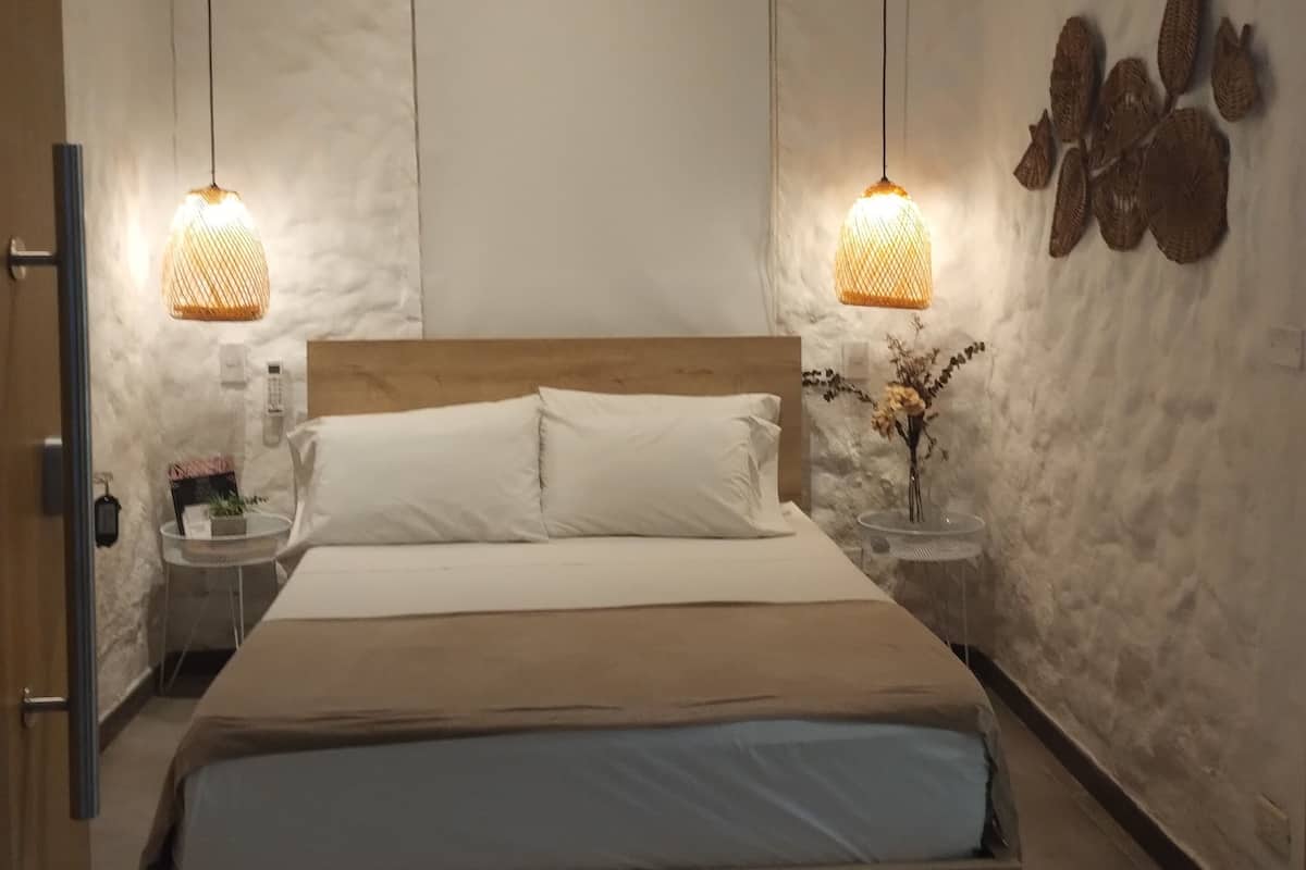 Ein Schlafzimmer mit einem Holzbett, weißer Bettwäsche, zwei Nachttischlampen, einer Klimaanlage und Wanddekoration mit Struktur.