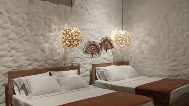 Une chambre avec deux lits, du linge de lit blanc et un mur blanc à la texture particulière.