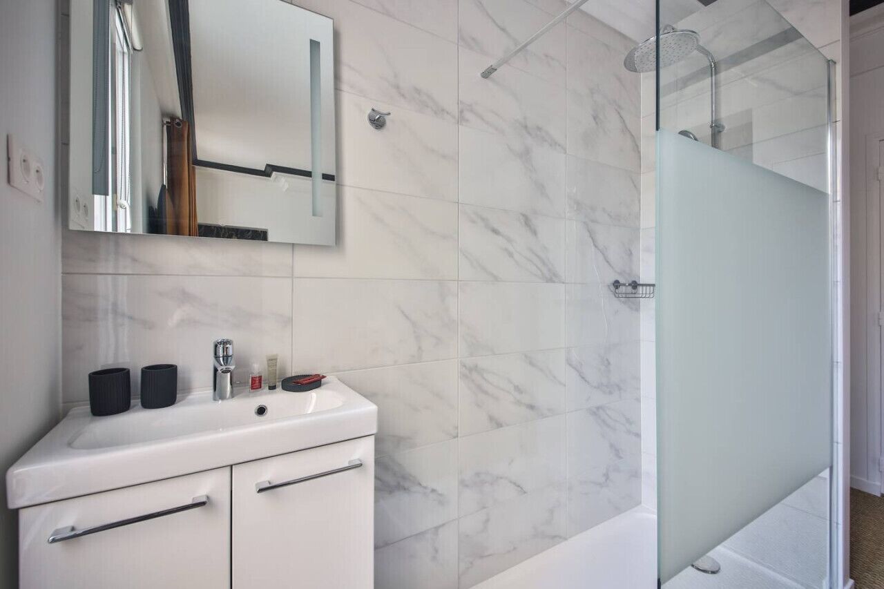 A modern bathroom with a white sink, mirror, and glass shower enclosure.