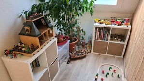 A playroom with a wooden playhouse, a large potted plant, and a toy train set.