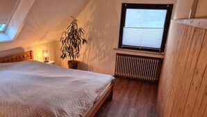 A bedroom with a bed, a radiator, a window with blinds, a potted plant, and a skylight.