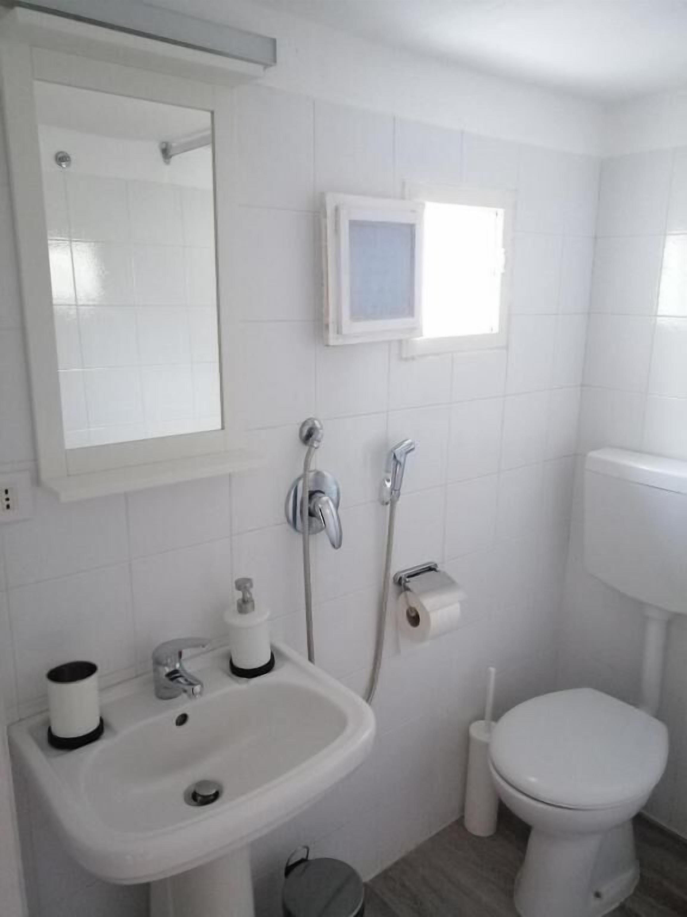 A bathroom with a white sink, mirror, toilet, and a small window.