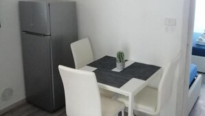 Una cocina pequeña y moderna con un refrigerador, una mesa de comedor con sillas y una pequeña planta en maceta.