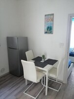 A small, modern kitchen with a refrigerator, a dining table with chairs, and a small potted plant.