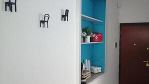 Un pasillo con un mueble azul para guardar objetos, una puerta de madera y dos sillas negras fijadas a la pared.