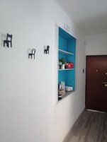 A hallway with a blue storage unit, a wooden door, and two black chairs mounted on the wall.