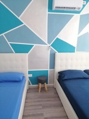 A bedroom with two beds, a small stool, and a wall-mounted air conditioner. - Newhouse 336 (Bari)