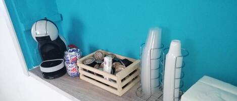 Een badkamer met een blauwgroene wand, een koffiezetapparaat, een krat met toiletartikelen en een handdoekhouder.