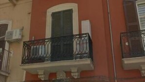 Un edificio con fachada roja, varios balcones con barandillas negras y una entrada central en arco.